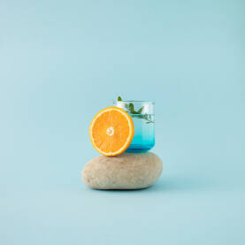 Ljetna pozadina s čašom vode i kriškom naranče na kamenu.
