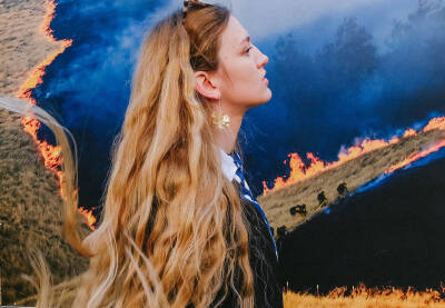 Djevojka duge plave kose stoji ispred plakata  na kome vatrogasci gase požar u prirodi. 
Sarajevo