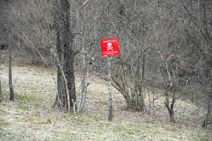 Upozorenje na minsko polje u šumi blizu linije fronta. Crveni znak minskog polja sa lobanjom i ukrštenim kostima. Znak upozorenja: Stop, opasno, nagazna mina. Pazi mine.