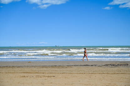 Žena šeta pješčanom plažom uz more ljeti.
