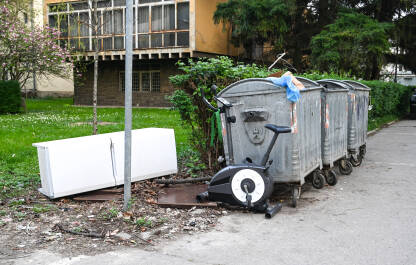 Kabasti otpad uz kontejnere za smeće u gradu. Smeće. Stari sobni bicikl i frižider u smeću.