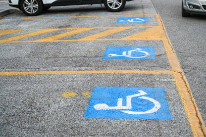 Znak za parkiranje rezervirano za osobe s invaliditetom na ulici. Simbol invalidskih kolica na asfaltu.