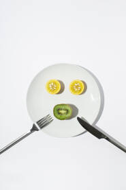 Prepolovljen limun i kivi na bijelom tanjuru s vilicom i nožem. Zdrava ishrana.