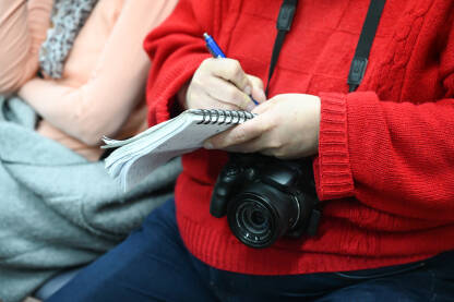 Novinar bilježi. Novinar sa foto-aparatom drži notes u ruci. Konferencija za štampu.