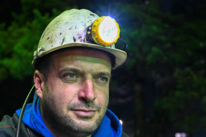 Portret rudara u rudniku. Rudar u radnom odijelu i s kacigom i svjetiljkom na poslu.