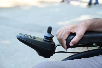Osoba sa invaliditetom upravlja invalidskim kolicima. Čovjek koji koristi džojstik za vožnju električnih invalidskih kolica, krupni plan.