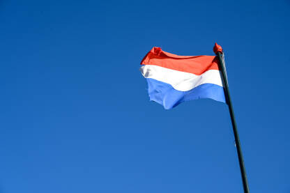Zastava Kraljevine Nizozemske. Holandska zastava se vijori na vjetru. Crvena, bijela i plava boja na holandskoj zastavi na plavom nebu.