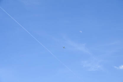 Avion na plavom nebu među oblacima i tragovima aviona. Putovanje. Komercijalni mlazni avion koji leti na nebu s mjesecom u daljini.