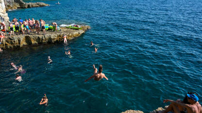 Mladić skače u more. Muškarac radi salto iznad vode. Mladi se zabavljaju na plaži i u moru kod Pule. Ljetni praznici.