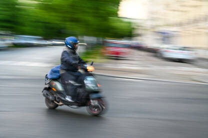 Čovjek se brzo kreće na motociklu na ulici. Vožnja skuterom po gradu. Vozač motocikla. Blurana fotografija.
