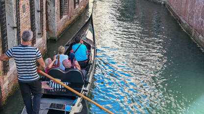 Venecija, Italija: Gondola na rijeci. Istorijske građevine uz riječni kanal. Popularna turistička destinacija. Turisti istražuju grad.