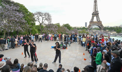 Pariz, Francuska: Ulični zabavljači zabavljaju grupu ljudi. Turisti na trgu sa Eiffelovim tornjem u pozadini.
