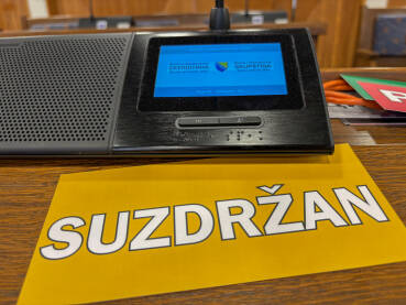 Sjednica u skupštini. Natpis SUZDRŽAN pored poslaničkog mikrofona.