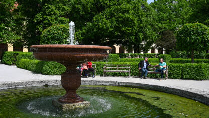 Fontana sa vodom u parku. Ljudi sjede na klupama u parku blizu fontane. Osvježenje tokom toplih ljetnih dana.
