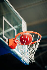 Fotografija košarkaški obruč s košarkaškom loptom u mreži. Obruč na staklenoj tabli. Lopta pri ulasku u koš. Slika iz niskog ugla, pozadina je zamućena.