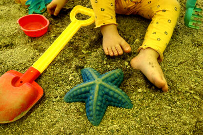 Dječije bose noge u pijesku, lopatica i morska zvijezda