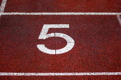 Broj pet. Brojevi na stazi za trčanje. Crvena staza za trčanje sa trakama i brojevima. Početne pozicije za trčanje na stadionu.