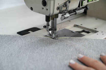 Žena šije tekstil šivaćom mašinom. Radnica radi u fabrici. Krupni plan djevojčinih ruku dok šije tkaninu u fabrici.