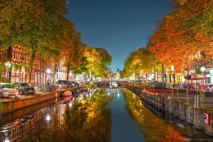 Zgrade, drveće i kanal u Amsterdamu noću. Grad Amsterdam, Holandija. Holandske kuće.