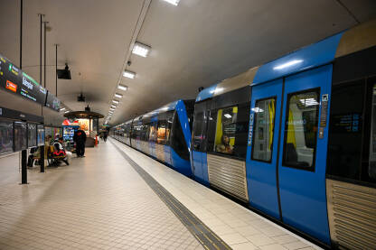 Putnici pored voza na modernoj podzemnoj željezničkoj stanici u Stockholmu. Putnici ulaze i izlaze iz metroa.