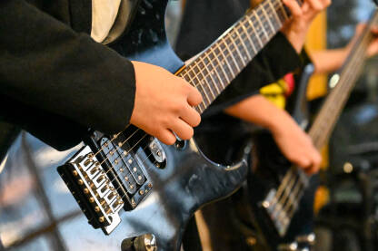 Mladi gitaristi sviraju električnu gitaru i bas gitaru na rock koncertu. Muzičar svira gitaru sa bendom na bini  na muzičkom festivalu.