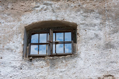 Prozor sa rešetkama kroz koji se vidi plavo nebo. Rustični zid stare zgrade