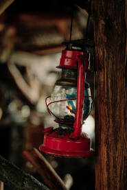 Crveni fenjer visi sa drvene grede u rustičnoj kolibi. Fenjer je čest prizor u mnogim ruralnim područjima, koristi se za osvetljavanje tokom noći.