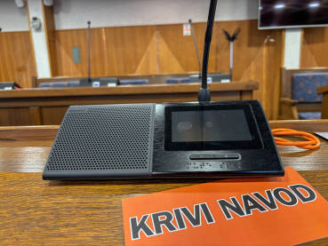 Sjednica u skupštini. Natpis KRIVI NAVOD pored poslaničkog mikrofona.