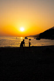 Scena sa mora: čovjek igra odbojku sa svojim djetetom na plaži pred zalazak sunca.