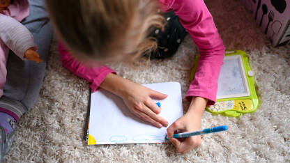 Djevojčica crta kod kuće. Obrazovanje djece. Djevojka piše i crta u svesci za domaći zadatak. Razigrana djeca.