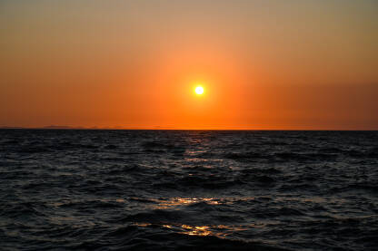 Sunce zalazi na narandžastom nebu na horizontu. Zlatni zalazak sunca na moru. Tropski zalazak sunca. Morski pejzaž i obala.