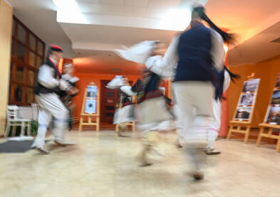 Zamućena fotografija grupe ljudi koji plešu. Muškarci i djevojke u tradicionalnoj narodnoj nošnji plešu. Tradicionalni ples. Kolo je južnoslovenski ples koji se izvodi na priredbama.
