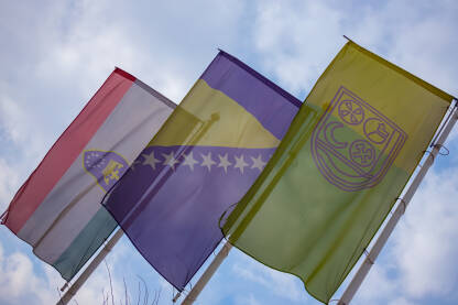 Zastave sa grbovima Grada Zenice, Zeničko-dobojskog kantona i zastava Bosne i Hercegovine snimljene pod uglom.