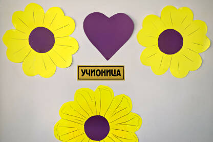 Ploča s oznakom učionice na vratima ukrašenim skupom cvjetova napravljenih od papira, sa srcem u središtu.