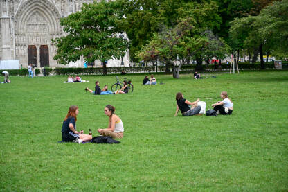 Mladi se druže na travi u parku. Ljudi sjede na zelenoj travi u parku.