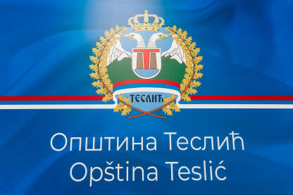 Grb Opštine Teslić na plavoj pozadini sa latiničnim i ćiriličnim natpisom Opština Teslić. Krupni kadar.