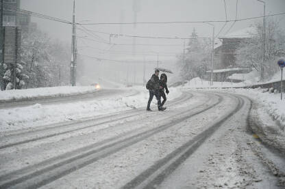 Ljudi prelaze ulicu pokrivenu snijegom.