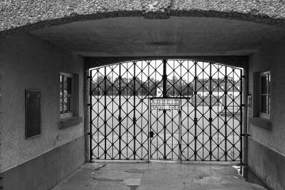 Ulazna kapija nacističkog koncentracionog logora Dachau, Njemačka. Ulazna kapija nacističkog koncentracionog logora Dachau, Njemačka. Memorijalni centar logora Dachau, crno bijela fotografija. Kapija logora sa natpisom "Arbeit macht frei" (prijevod: rad oslobađa).