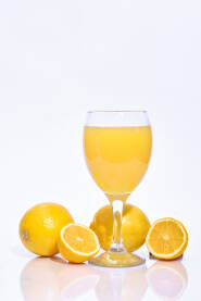 Cijele i narezane kriške limuna s čašom iscijeđenog soka na bijeloj pozadini