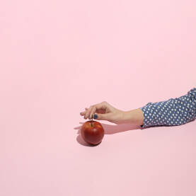 Ženska ruka drži peteljku svježe crvene jabuke.