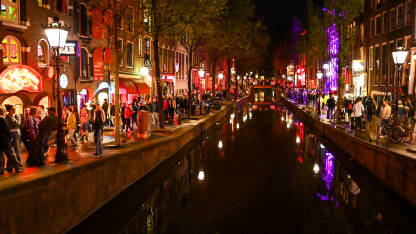 Amsterdam, Nizozemska. Red light district noću. Zgrade, riječni kanal i turisti u gradu.