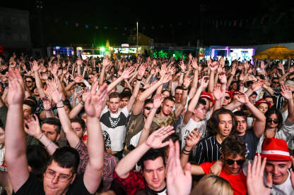 Grupa mladih ljudi pjeva i pleše na koncertu. Publika ispred bine na muzičkom festivalu. Ljubitelji muzike uživaju u rok koncertu.  Mostar summer fest.