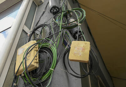 Žice i kablovi na fasadi zgrade Žice od telefona, interneta, kablovske televizije i drugih servisa umotani u veliko klupko na fasadi zgrade. Kablovi na ulazu u zgradu.
