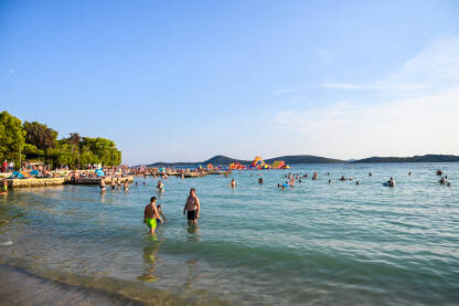 Ljudi u moru tokom turističke sezone. Prepuna plaža i more. Godišnji odmor. Turisti na odmoru na Jadranu.