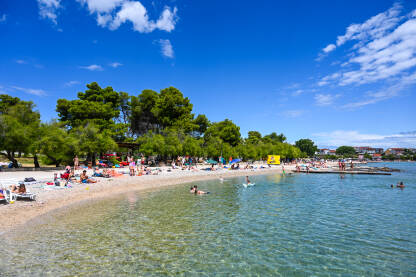Vodice, Hrvatska: Turisti na moru. Ljudi plivaju u moru. Prepuna plaža. Turisti se sunčaju na plaži. Ljetni odmor. Grupa turista na plaži tokom toplog dana ljeti.