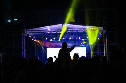 Siluete ljudi koji prate koncert uživo s osvijetljenim LED pozadinskim ekranom. Grupa ljudi na muzičkom festivalu.