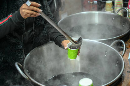 Žena sipa vruće kuhano vino na božićnom sajmu. Vruće začinjeno vino na prazničnom sajmu.
