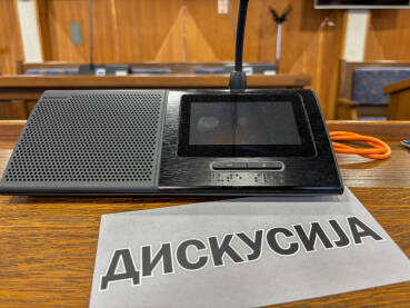 Sjednica u skupštini. Natpis DISKUSIJA pored poslaničkog mikrofona.