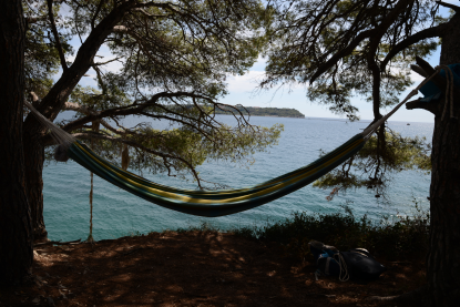 Ležaljka hemok špagom vezana za drvo. Ruksak za putovanja. Odmaranje na litici pored mora na Istri.