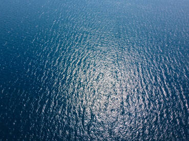 Površina plavog mora, snimak dronom. Odraz sunca na površini vode. Valovi na moru. Duboko plavo more.